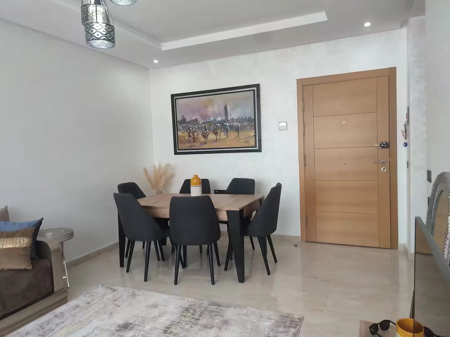 Salle à manger claire d'un appartement à Agadir, avec table en bois, chaises noires et tapis à motifs