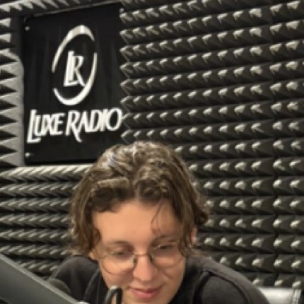 Reda du Réseau au micro dans le studio de Luxe Radio, devant le logo de la station